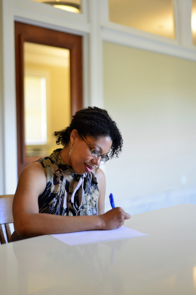 Mariam Williams, sitting at a table, pen in hand